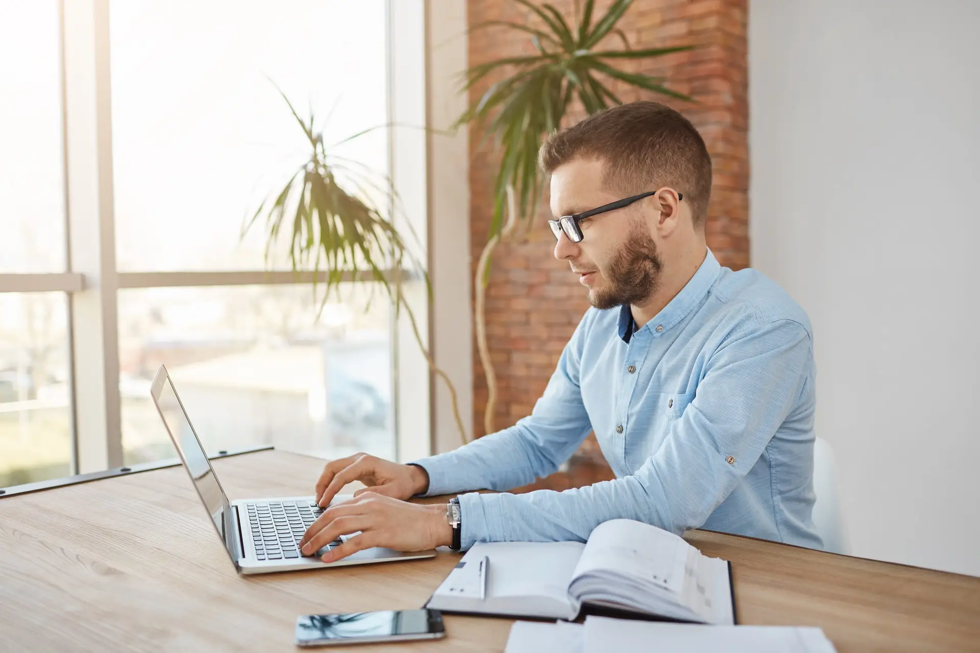 closw up portrait of adult concentrated unshaven male company accountent in glasses and shirt sitting in comfortable office working on laptop computer.
